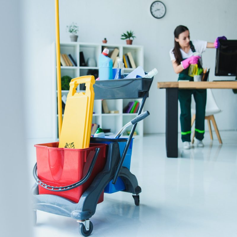 young-female-janitor-cleaning-office-with-various-cleaning-equipment