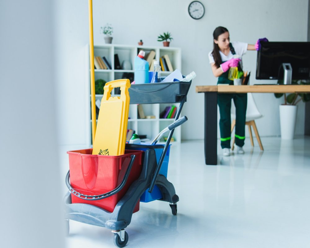 young-female-janitor-cleaning-office-with-various-cleaning-equipment