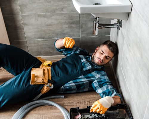 bearded handyman lying on floor near toolbox in bathroom