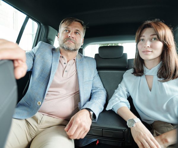 Affectionate happy middle aged husband and wife in casualwear sitting on backseat of new model of car during test drive and looking forwards