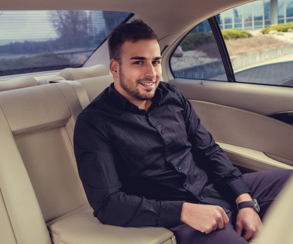 Smiling bearded man in a black shirt sitting in the car.