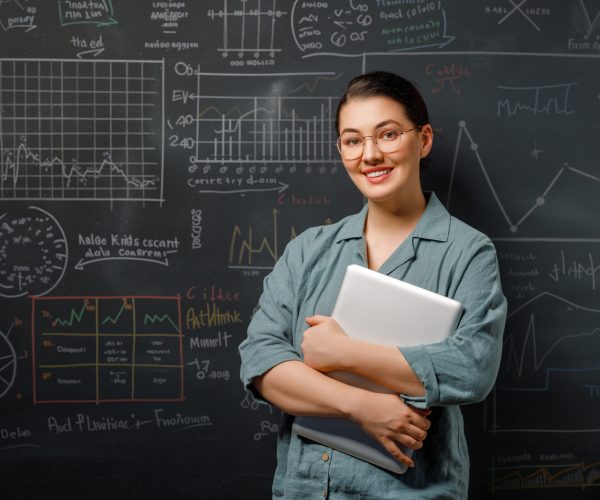 Back to school. Happy teacher indoors. Woman is standing in class on background of blackboard.