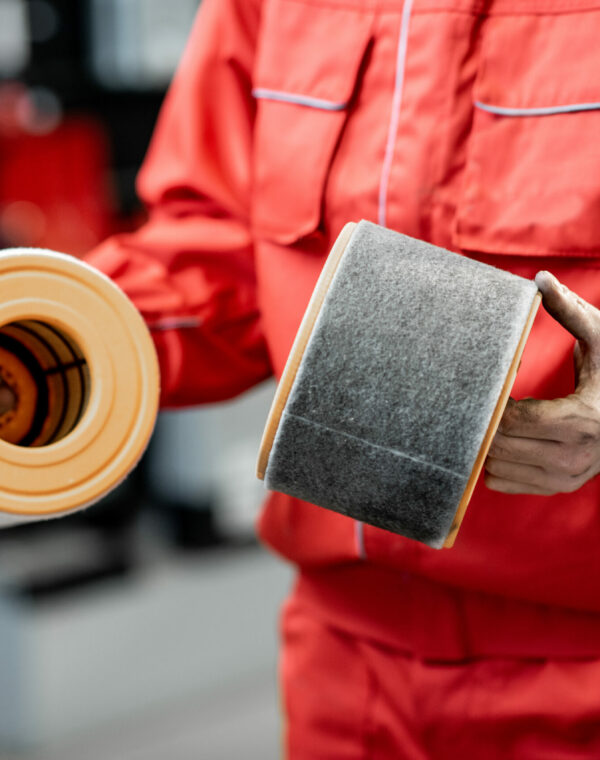 Auto mechanic in red uniform holding new and used air filter standing at the car service, close-up view with no face