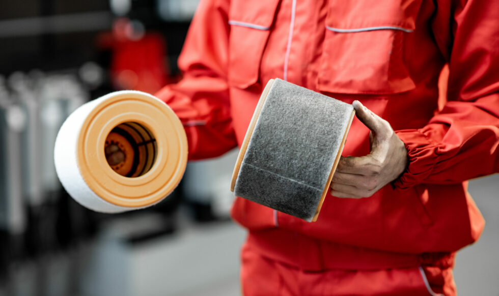Auto mechanic in red uniform holding new and used air filter standing at the car service, close-up view with no face