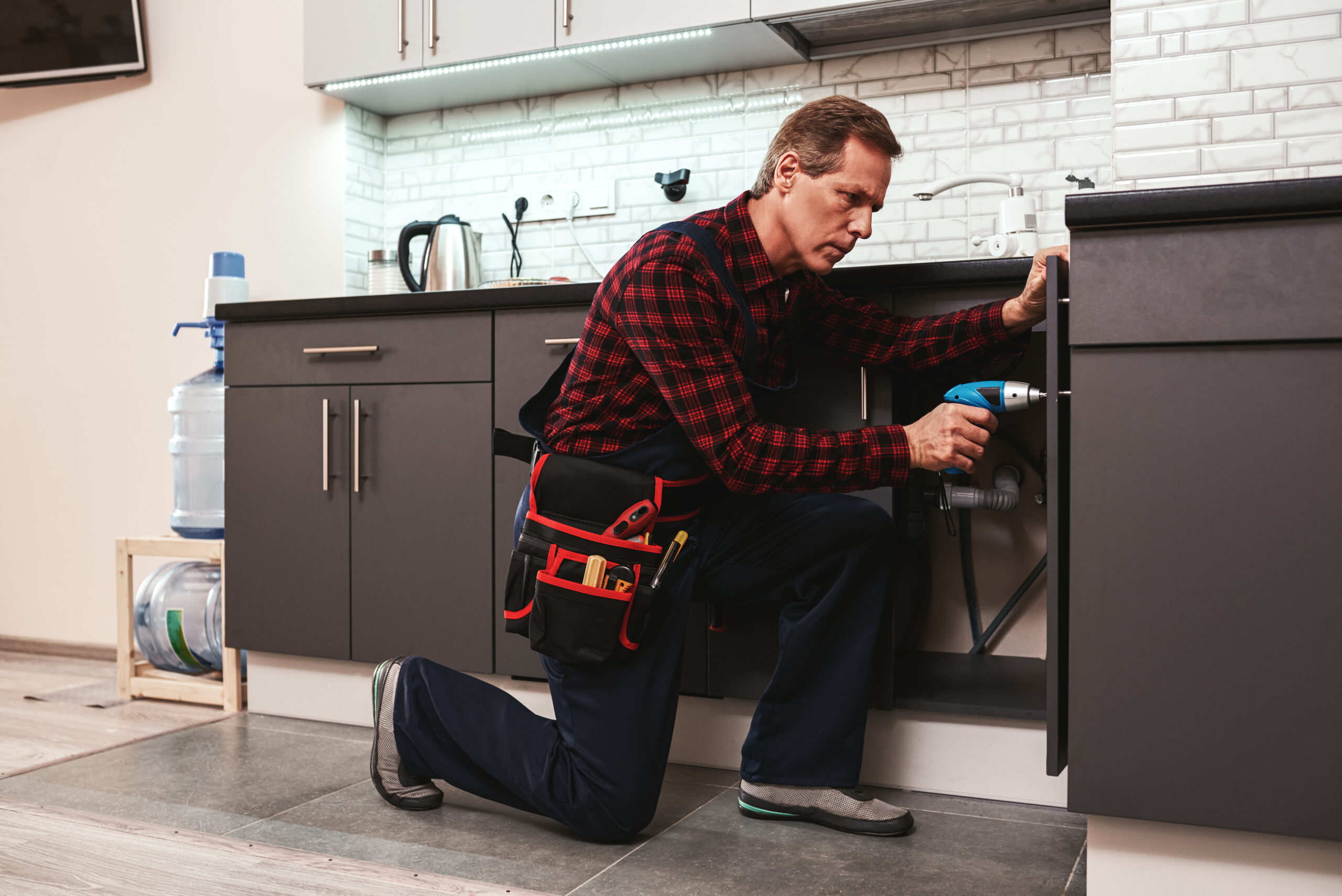 Handyman at work. Repairing kitchen shelves by perforator. Artisan senior adult man trying to fix kitchen shelves